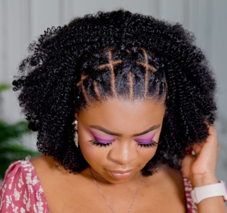 Close-up of a woman with criss-cross flat twists at the front and a defined 4B twist-out, eyes down, soft glam makeup.